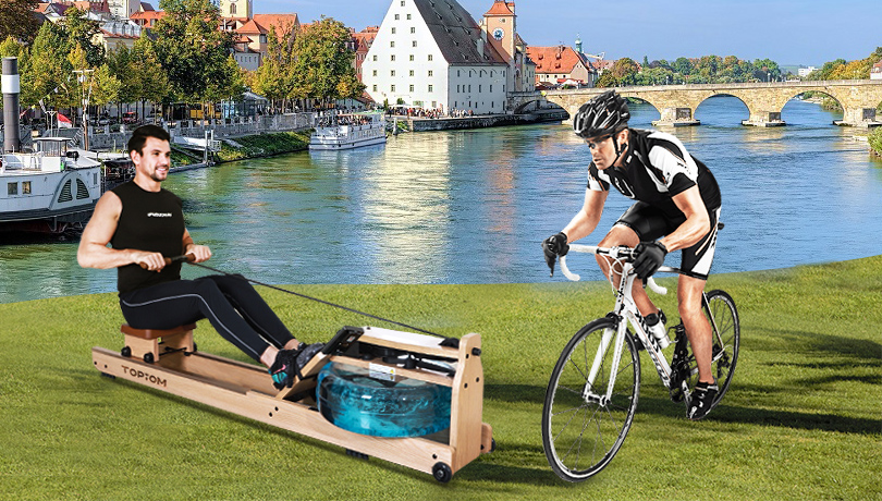 one man rows with a rowing machine and another man rides a bike near a lake