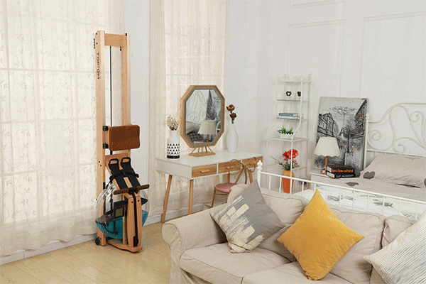 Topiom rowing machine tilted upright against a white curtain in a bedroom