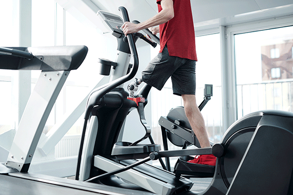 a person wearing a red shirt grips the handlebars of an elliptical trainer