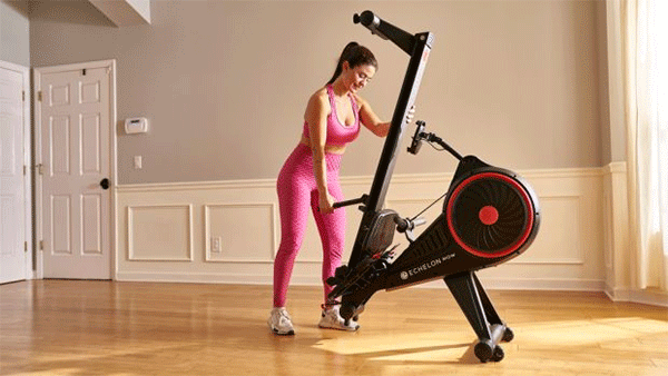 a woman wearing pink trousers folds Echelon magnetic rowing machine