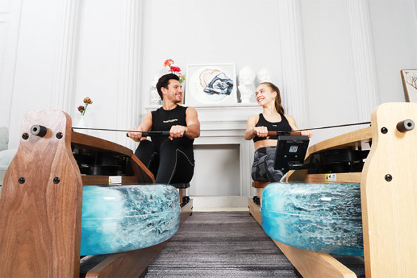 a man rowing with a water rowing machine while smiling at a women rowing with another water rowing machine