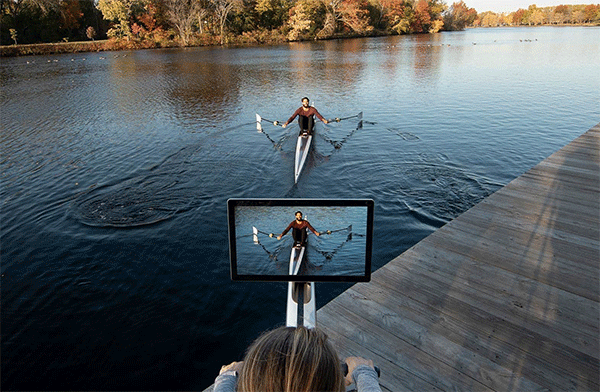 one person looks at the monitor screen and another person in the screen row on a lake