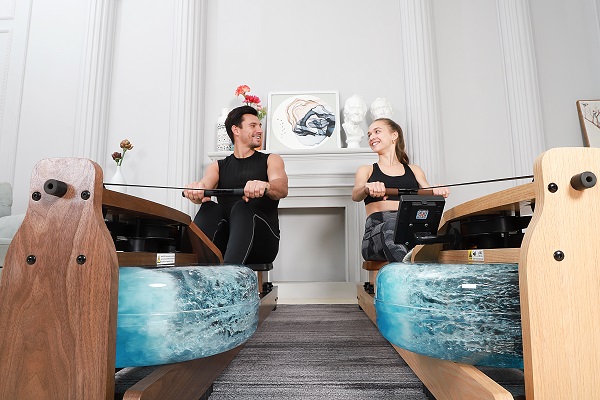 a man rowing with a water rowing machine while smiling at a women rowing with another water rowing machine