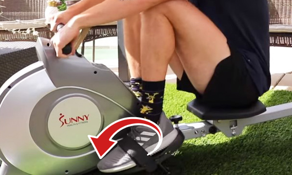 A person sits on a rowing machine with toes pointing downwards