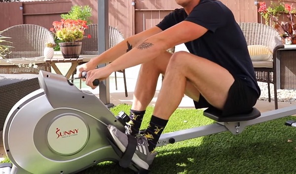 A person sits on a rowing machine with heels pointing downwards
